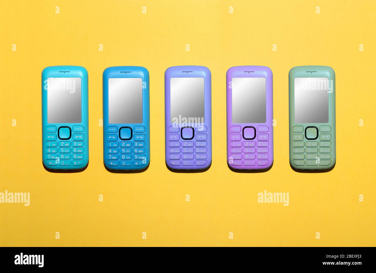 Fünf verschiedene Farben von Mobiltelefonen mit leeren Bildschirmen in einer Linie über einem hellen gelben Hintergrund mit Kopierraum unten Stockfoto