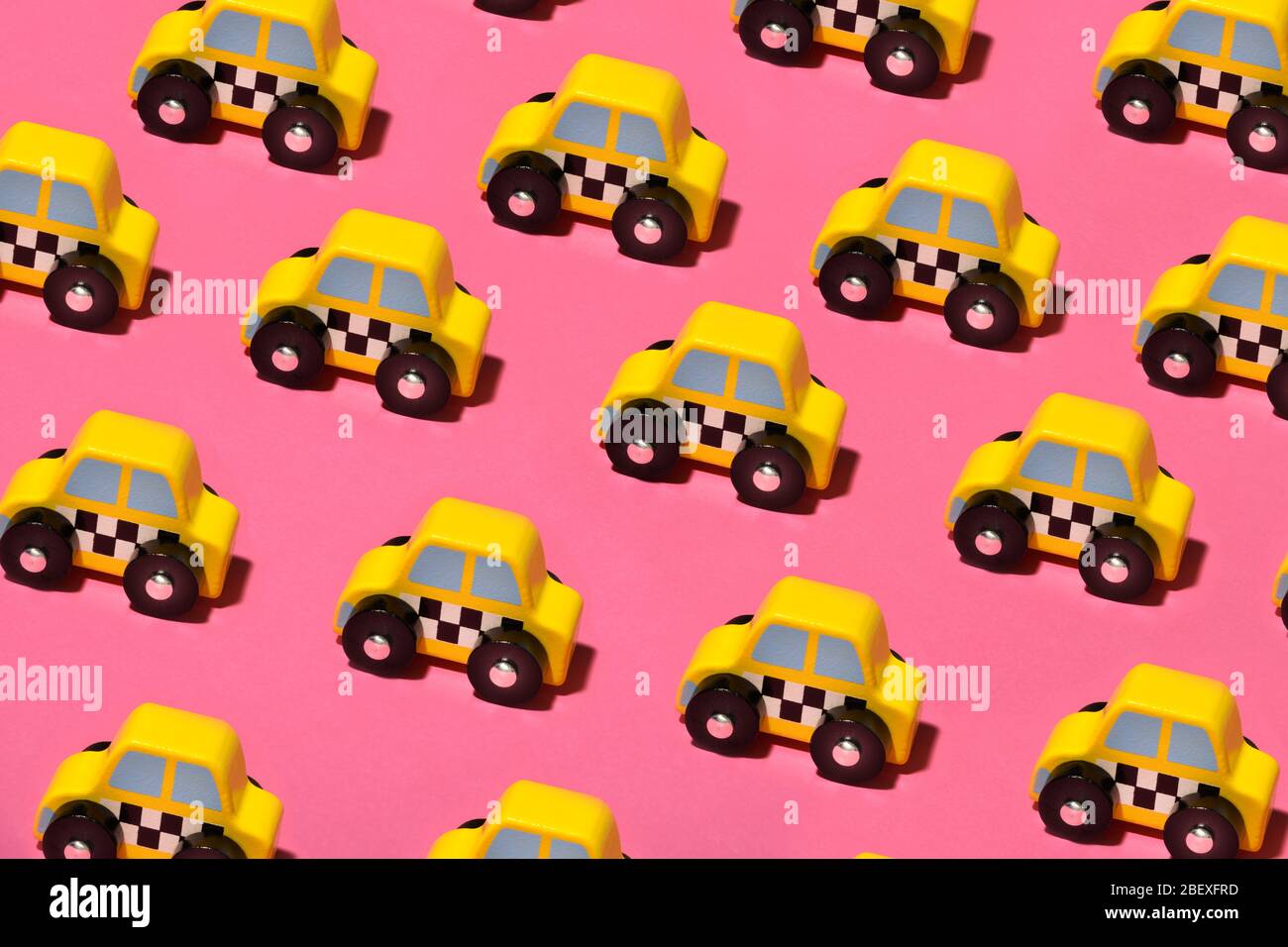 Reihen von kleinen gelben Spielzeug Taxis oder Taxis auf einem bunten rosa Hintergrund gesehen hohen Winkel im Vollformat Stockfoto