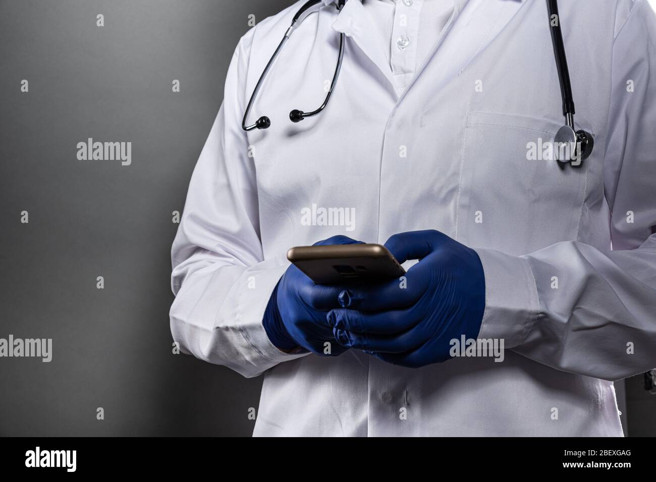 Arzt in weißer Uniform und Schutzhandschuhe mit Smartphone Stockfoto