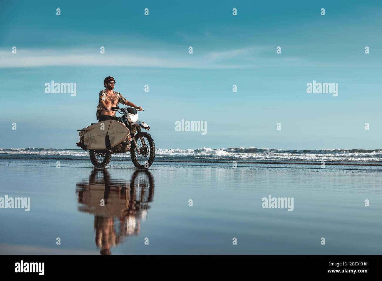 Echte Bali Male Surfer fährt auf Motorrad mit Surfbrett am Meeresstrand Stockfoto