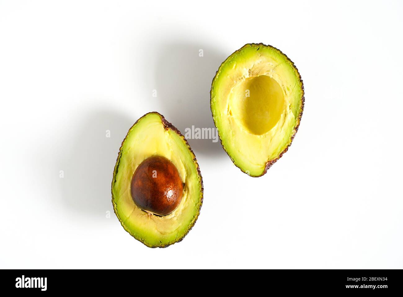 Ein Avocado, das in zwei Hälften geschnitten wurde, um den Kern vor einem weißen Hintergrund zu enthüllen Stockfoto
