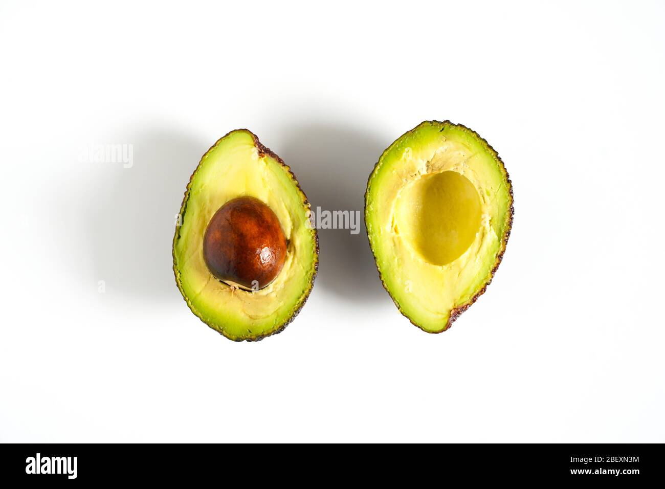 Ein Avocado, das in zwei Hälften geschnitten wurde, um den Kern vor einem weißen Hintergrund zu enthüllen Stockfoto