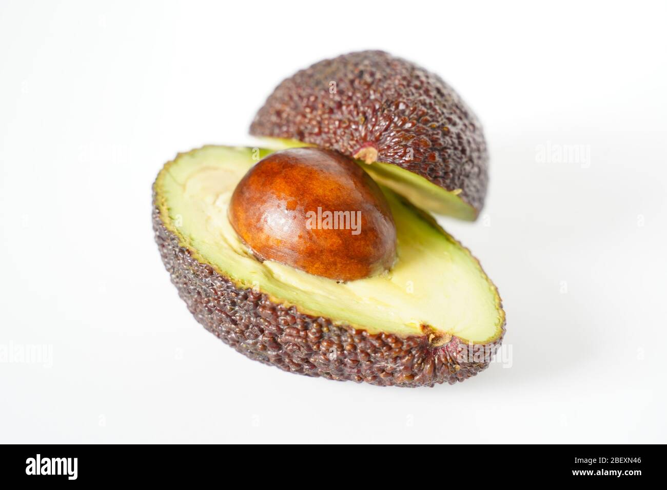 Ein Avocado, das in zwei Hälften geschnitten wurde, um den Kern vor einem weißen Hintergrund zu enthüllen Stockfoto