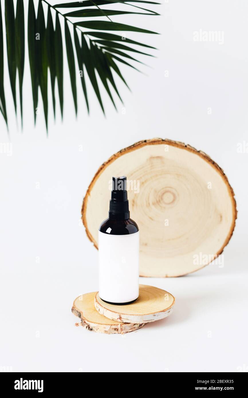 Glassprühflasche auf einem Holztablett auf weißem Hintergrund, umgeben von Palmblatt. Stockfoto