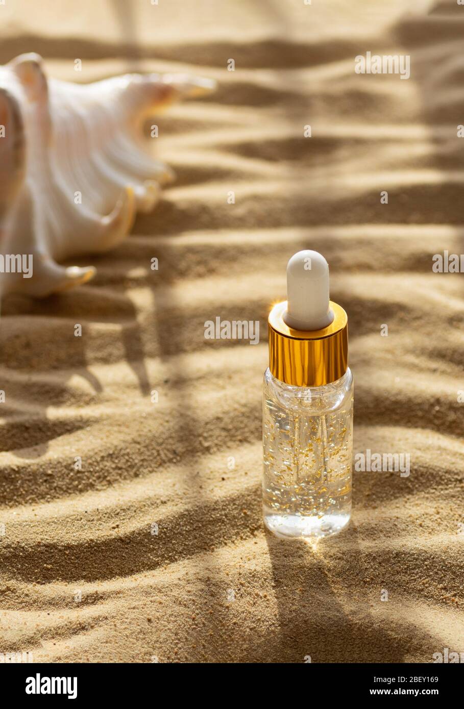 Feuchtigkeitsspendende Gesichtsbehandlung in einer transparenten Flasche auf einem Hintergrund aus Meersand. Nahaufnahme. Vertikales Beschneiden. Stockfoto