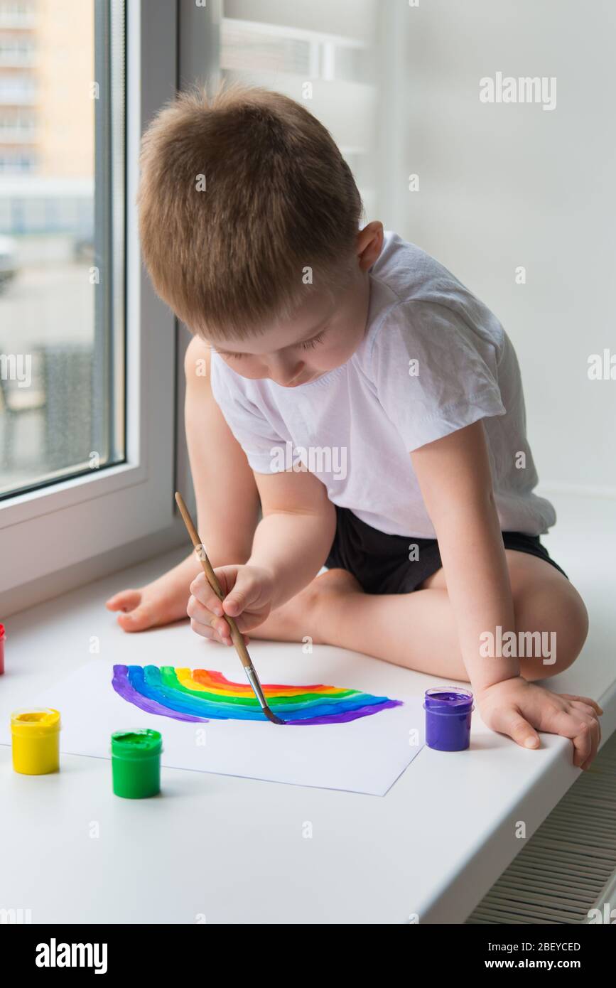 Der Junge, der auf der Fensterbank sitzt, zeichnet den Regenbogen für das Projekt Chasetherainbow Stockfoto