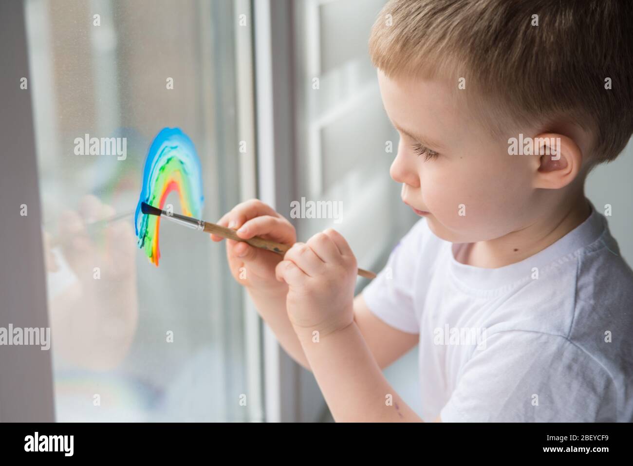 Lasst uns alle gut sein. Kind zu Hause zeichnet einen Regenbogen auf das Fenster. Flash Mob Chasetherainbow auf Selbstisolierung Quarantäne Pandemie Coronavirus. Stockfoto