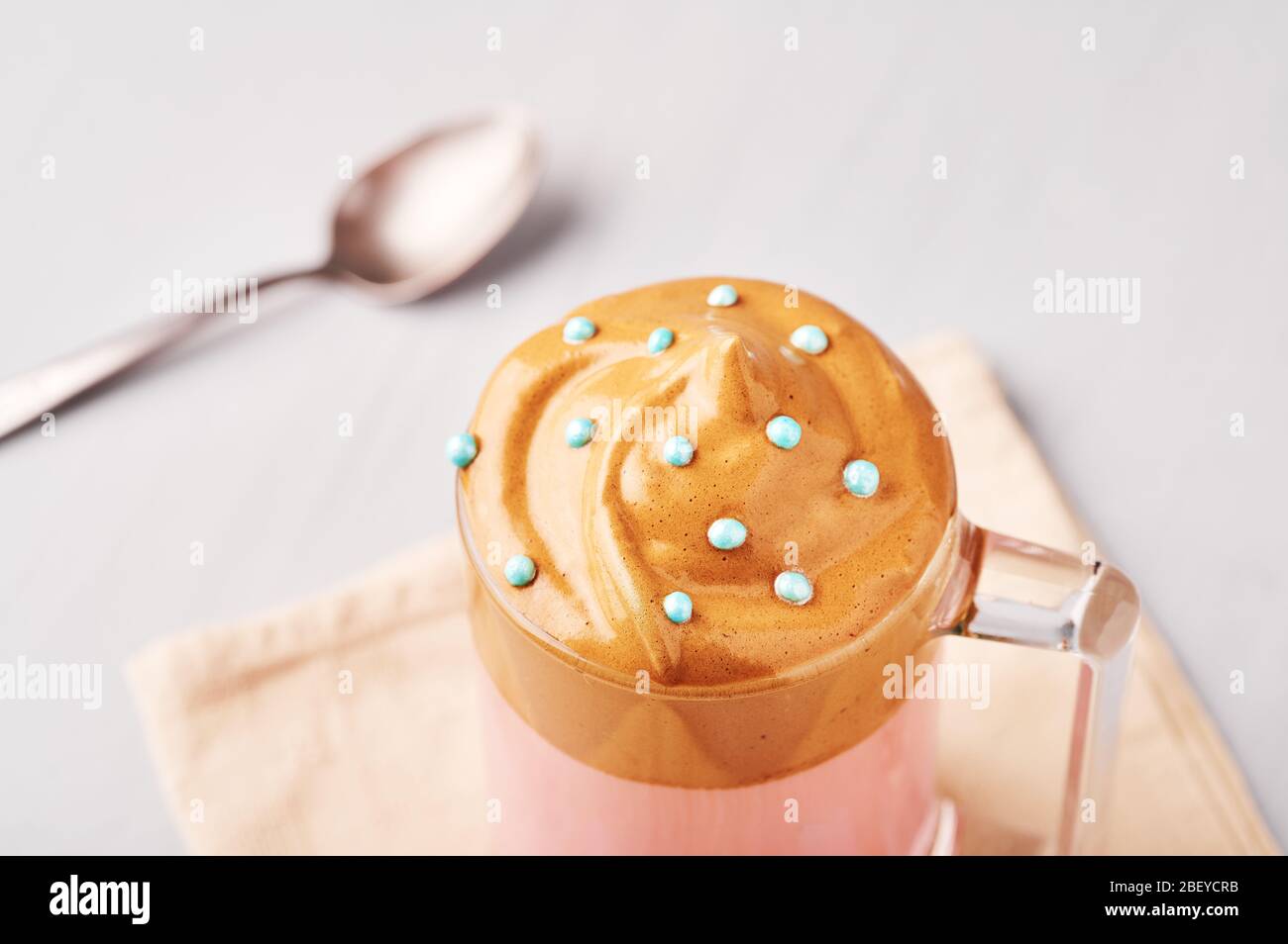 Pink Milk Dalgona Kaffee mit blauen Ostern Streusel in einem Glas Tasse auf hellgrauen Hintergrund dekoriert. Dalgona Schaumkaffee ist ein koreanisches Trendgetränk Stockfoto