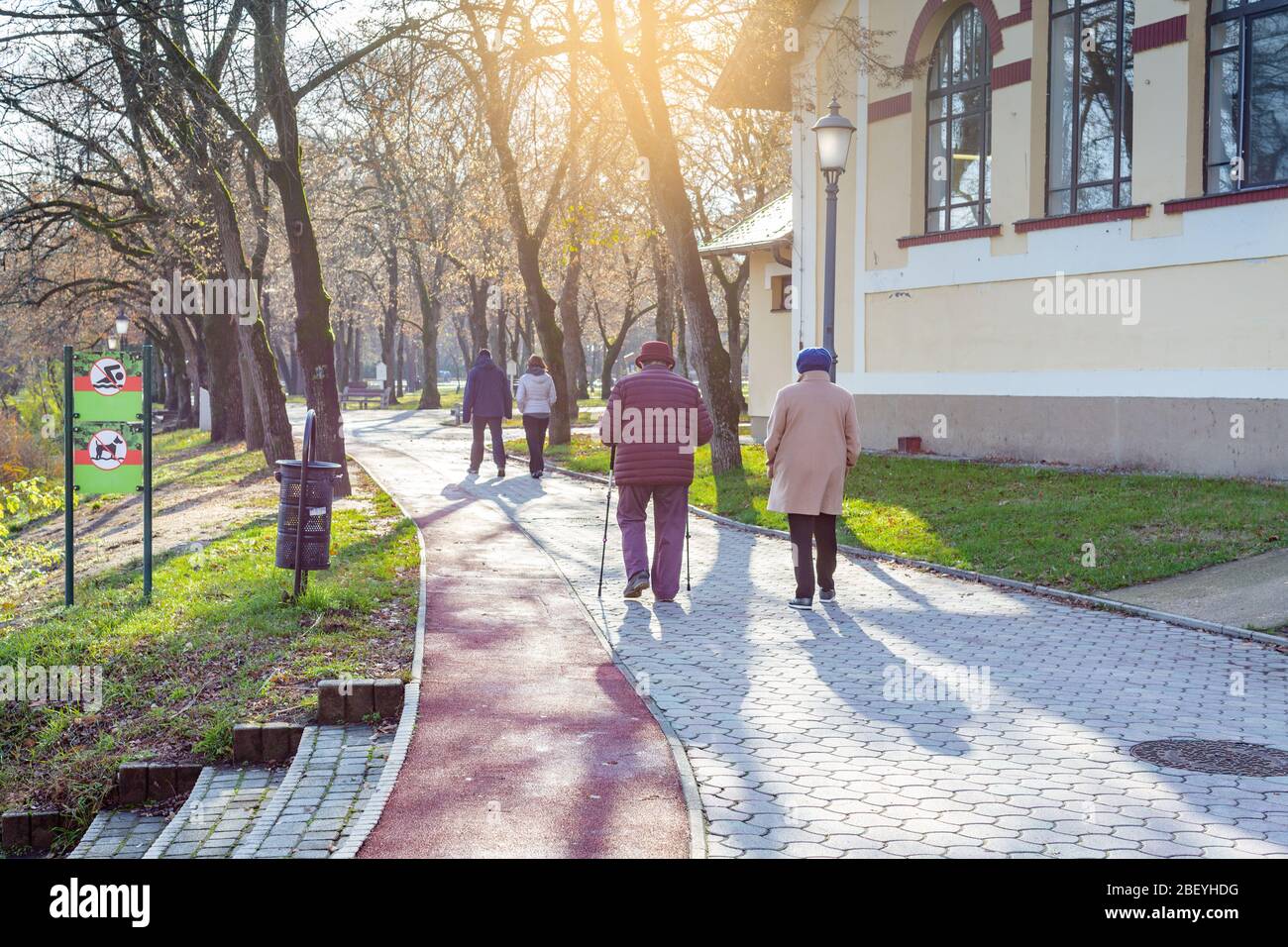 Ältere Frauen und junge Paare gehen auf dem Parkweg entlang. Eine der Frauen, die Nordic Walking Stöcke verwenden. Nyiregyhaza, Ungarn Stockfoto