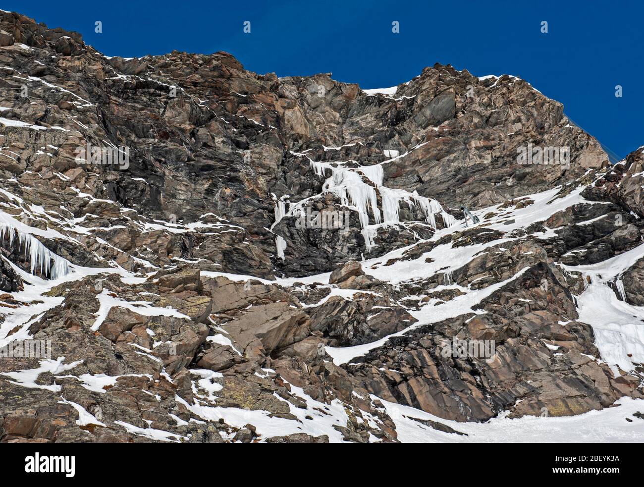 Zerklüftete alpine Felslandschaft mit gefrorenem Wasserfall, der mit Schnee und Eis bedeckt ist Stockfoto