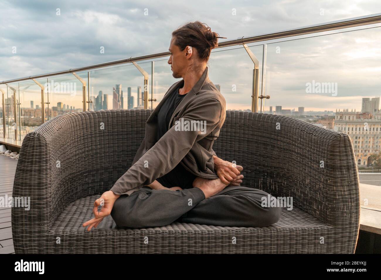 Junger Mann in Lotus Pose auf dem Dach Blick auf die Stadt von oben und entspannen von Stress in Quarantäne und Isolation von Coronavirus Pandämie, halten Social D Stockfoto