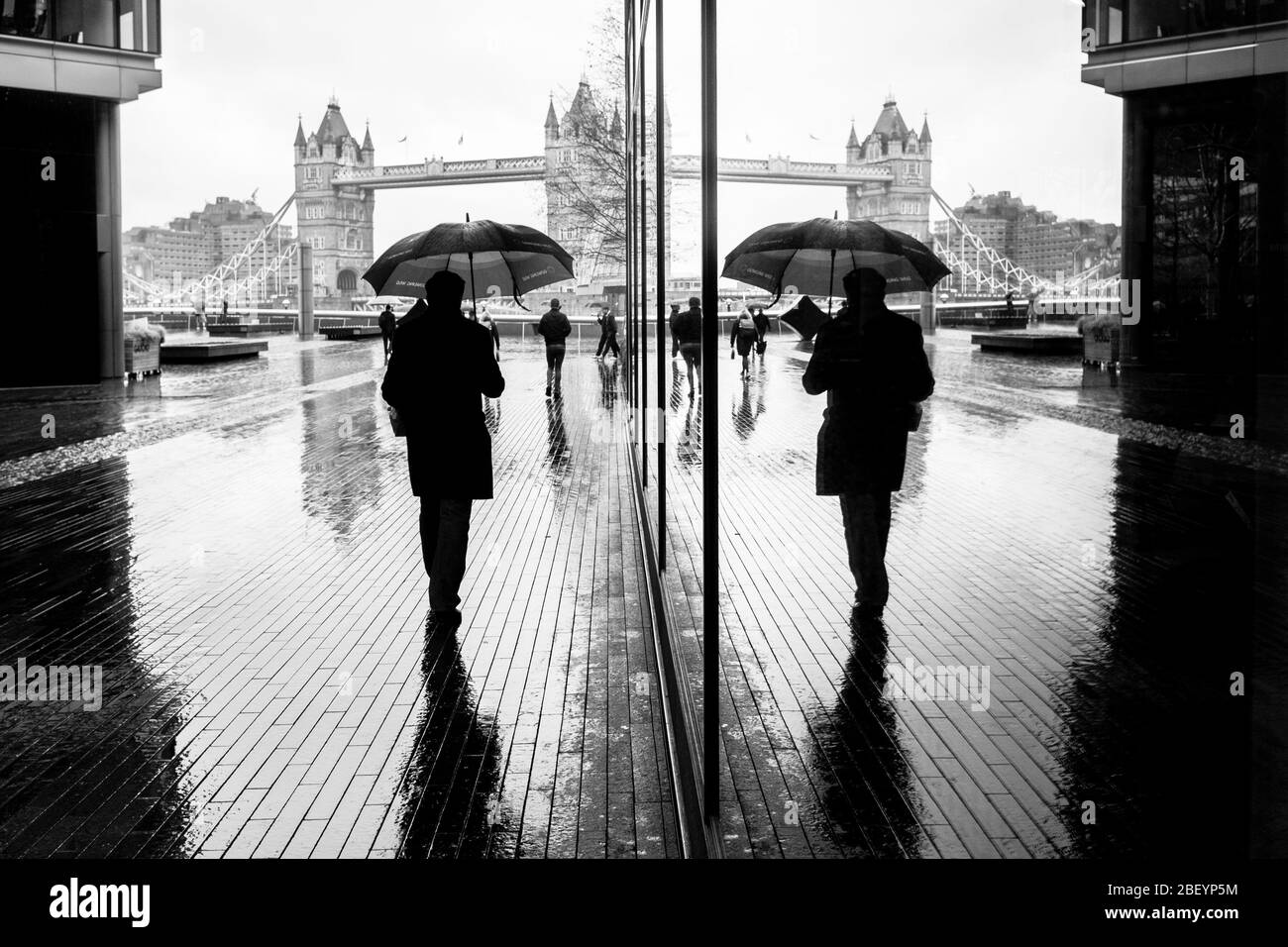 London schwarz-weiß-Straßenfotografie: Mann mit Regenschirm und Tower Bridge Reflexion. Stockfoto