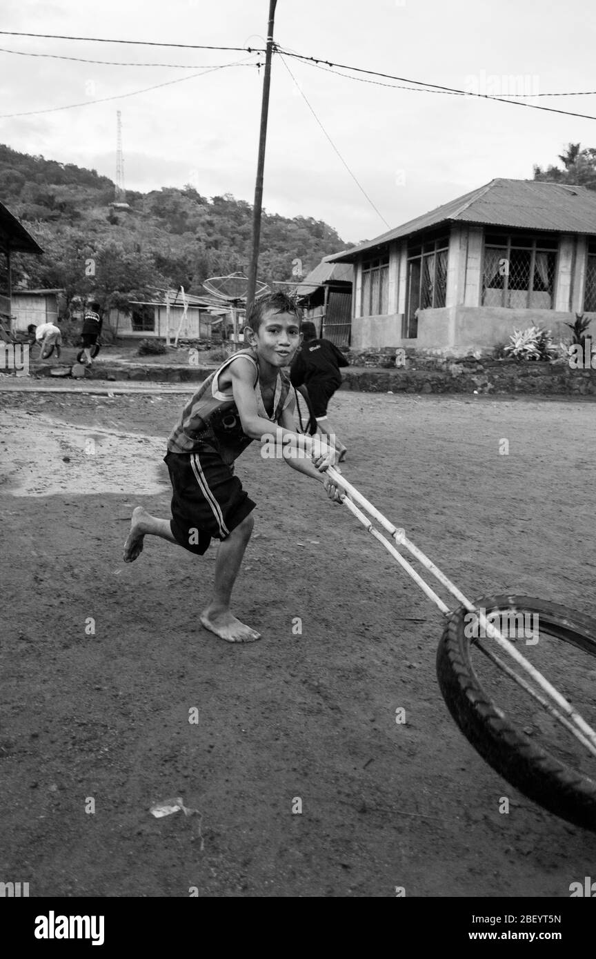 Kelimutu, East Nusa Tenggara / Indonesien - Januar 13 2015: Porträt eines Jungen in einem traditionellen Dorf, der mit einem Rad als Spielzeug spielt. Schwarz und Weiß Stockfoto