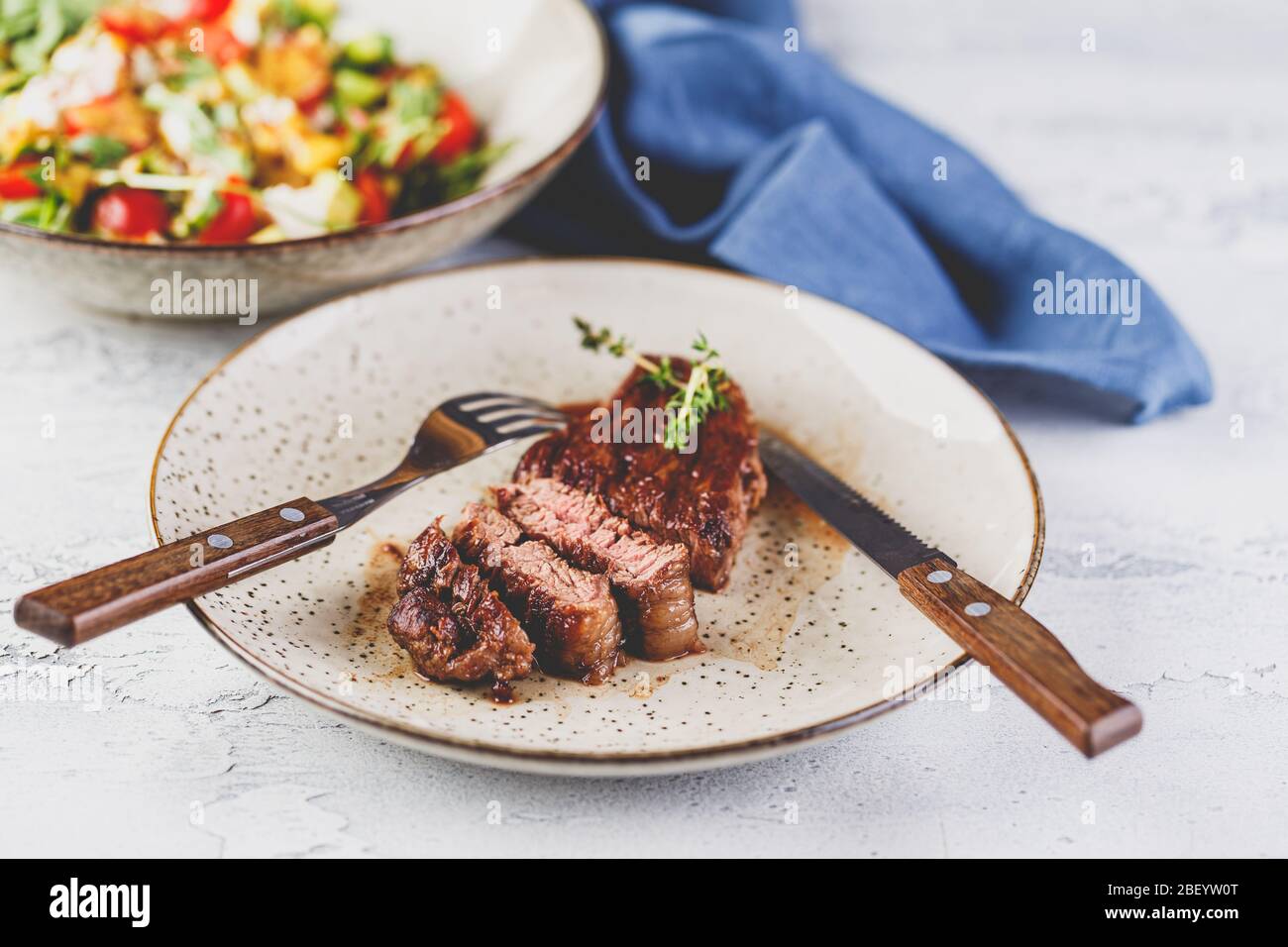 Gegrilltes Steak und Gemüsesalat in Scheiben auf hellem Hintergrund. Tischeinstellung, Speisekonzept. Stockfoto