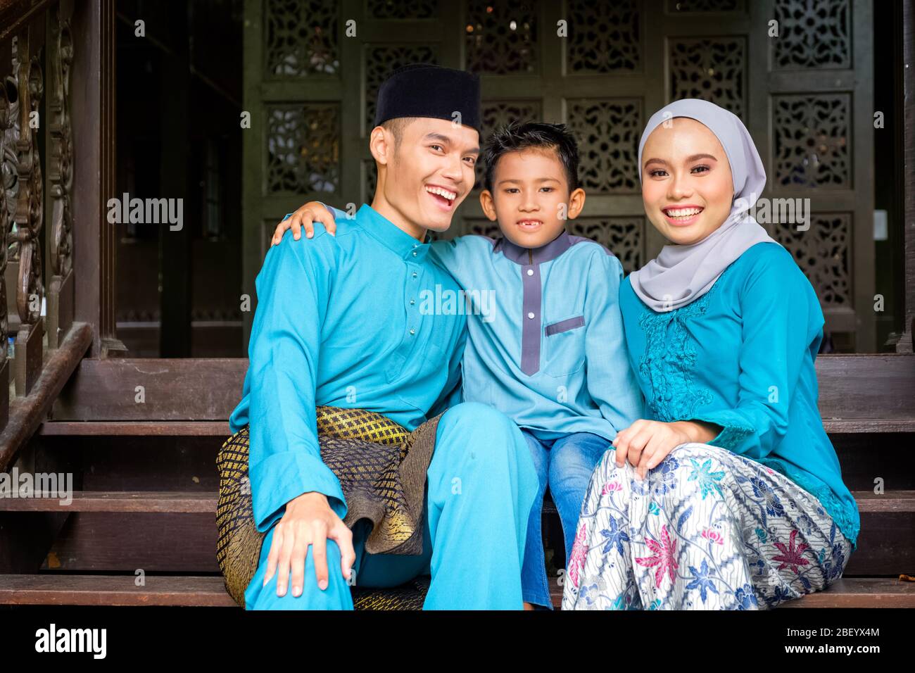 Ein Porträt des jungen Paares des malaiischen muslim in traditioneller Tracht mit seinem Sohn während der Eid al-Fitr Feier durch traditionelles Holzhaus. Raya und Mu Stockfoto