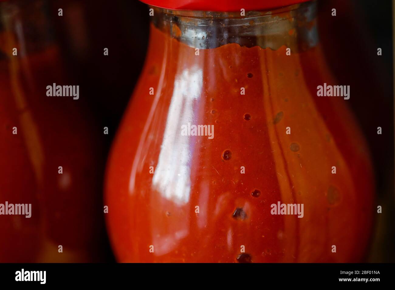 Geringe Schärfentiefe (selektiver Fokus) Details mit Tomatenmark in einer Glasflasche auf dem Regal in der Speisekammer. Stockfoto