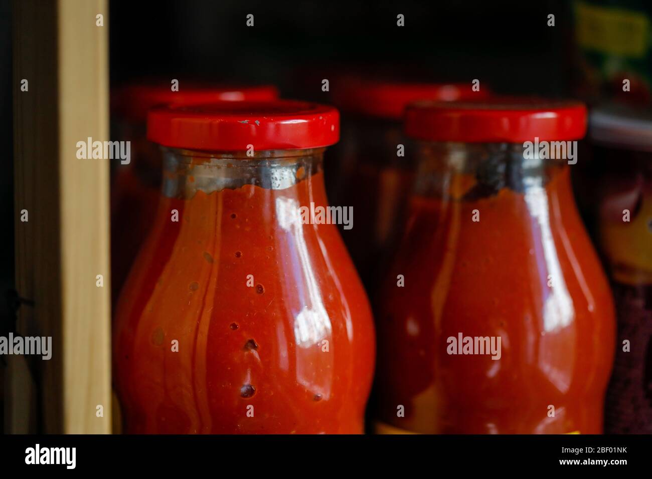 Geringe Schärfentiefe (selektiver Fokus) Details mit Tomatenmark in einer Glasflasche auf dem Regal in der Speisekammer. Stockfoto