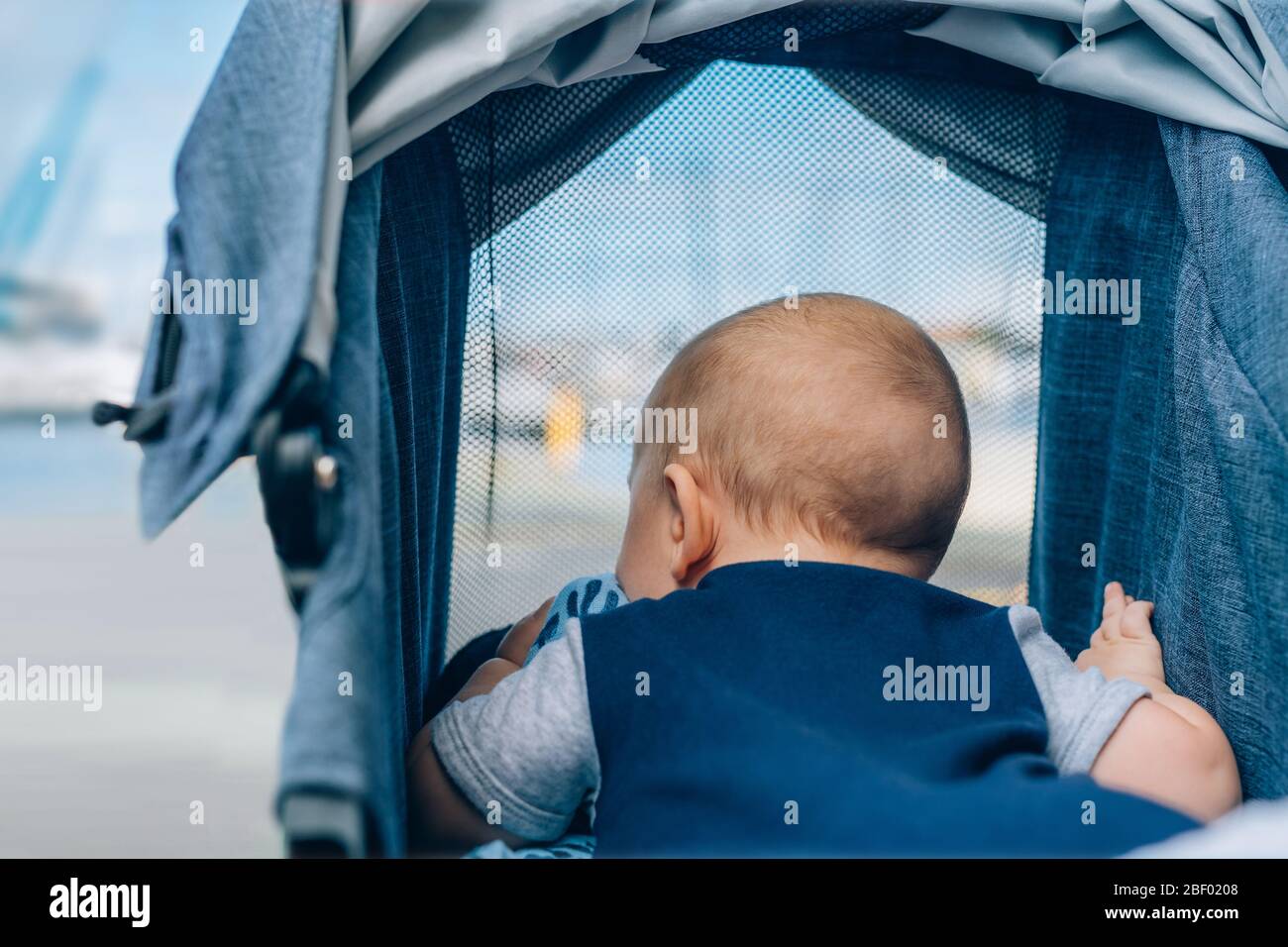 Kleiner Junge im Kinderwagen, der durch das Netzfenster auf die Marina Bay schaut. Stockfoto