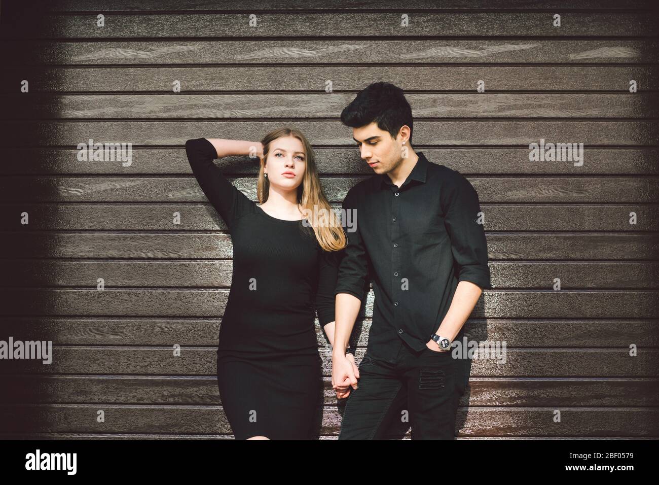 Multirassisches stilvolles Paar in schwarzer Kleidung posiert auf einem Hintergrund einer Holzwand. Türkisch Kerl und kaukasische Frau Datum und Liebe. Lifestyle Elegant Stockfoto