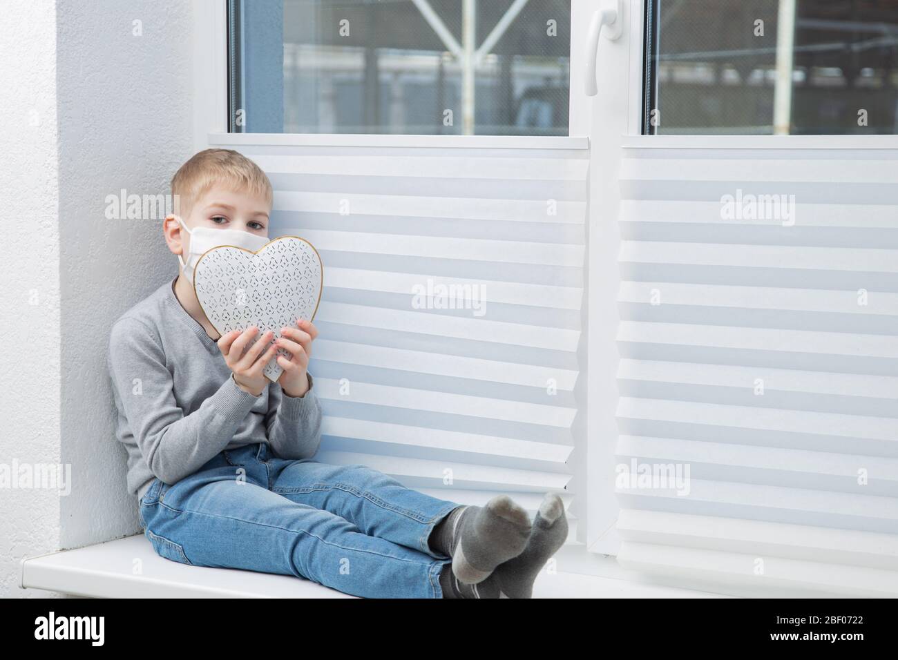 Junge tragen Schutzmaske sittin auf der Fensterbank spielen Tablette Stockfoto