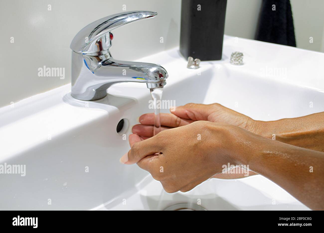 Schwarze Frau, die ihre Hände gewissenhaft mit Wasser spült. Selektiver Fokus auf Hände. Desinfektion. Hygienekonzept. Stockfoto