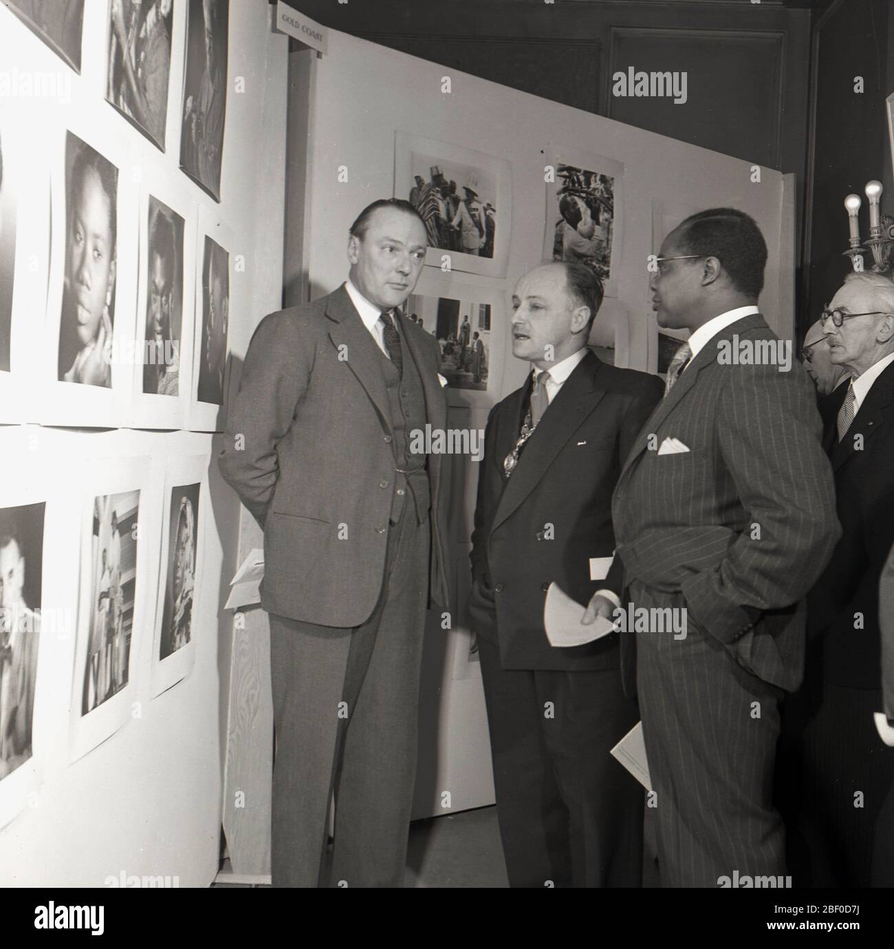 1950, historische, passende Gäste auf einer Fotoausstellung, die eine Auswahl von Bildern von der afrikanischen Goldküste aus dieser Zeit diskutiert, London, England, Großbritannien. Die Goldküste in Westafrika war von 1821 bis zu ihrer Unabhängigkeit 1957 eine britische Kolonie. Stockfoto