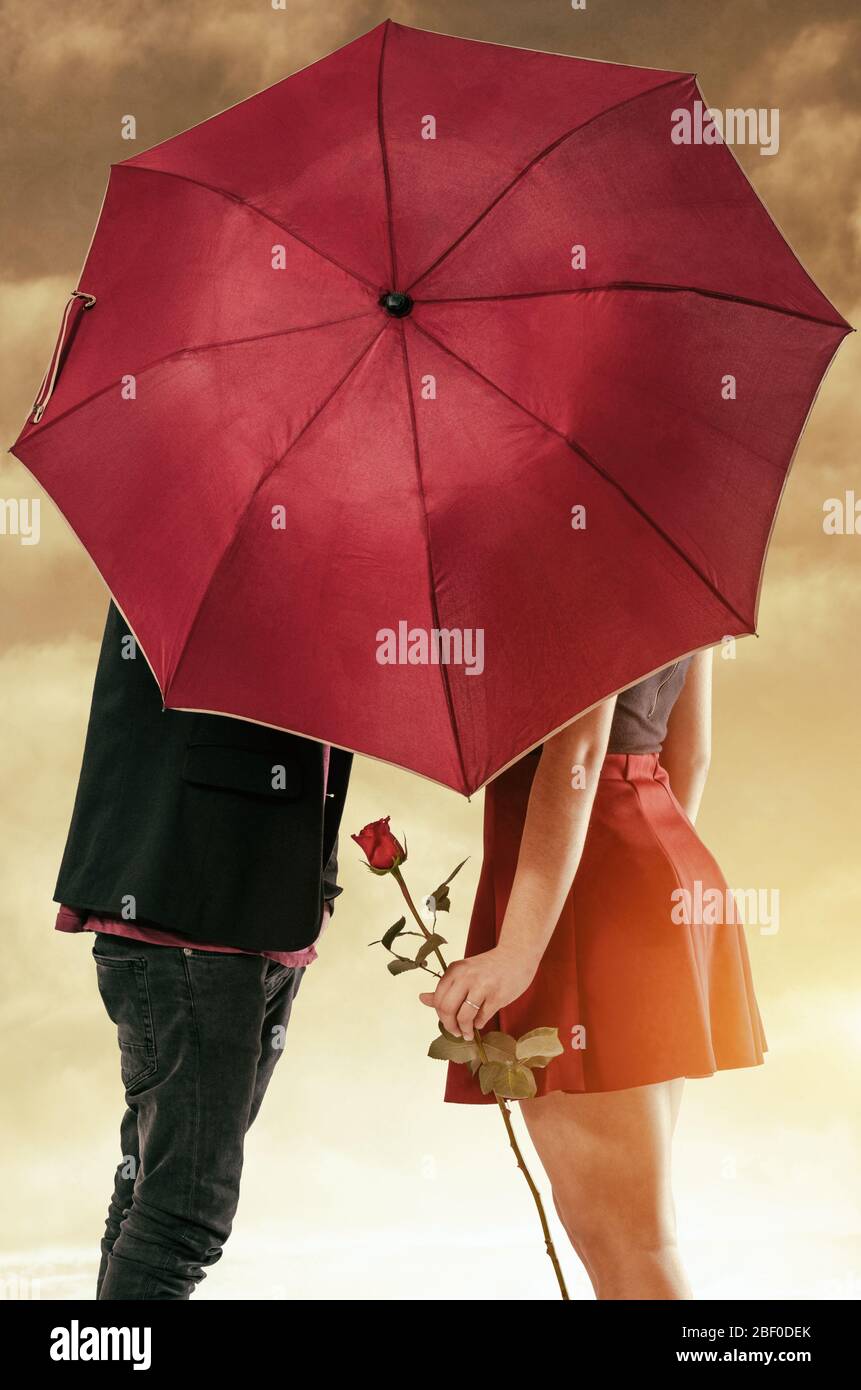 Freundin und Freund mit einem leidenschaftlichen Kuss hinter dem Regenschirm versteckt Stockfoto