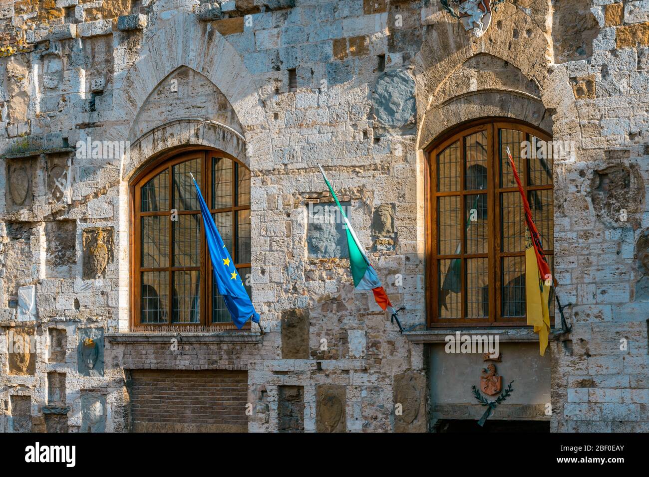 San Gimignano, Toskana: Zwei Fenster und Flaggen an der Fassade des mittelalterlichen Palazzo Comunale (oder Palazzo del Popolo) auf der Piazza del Duomo. Stockfoto