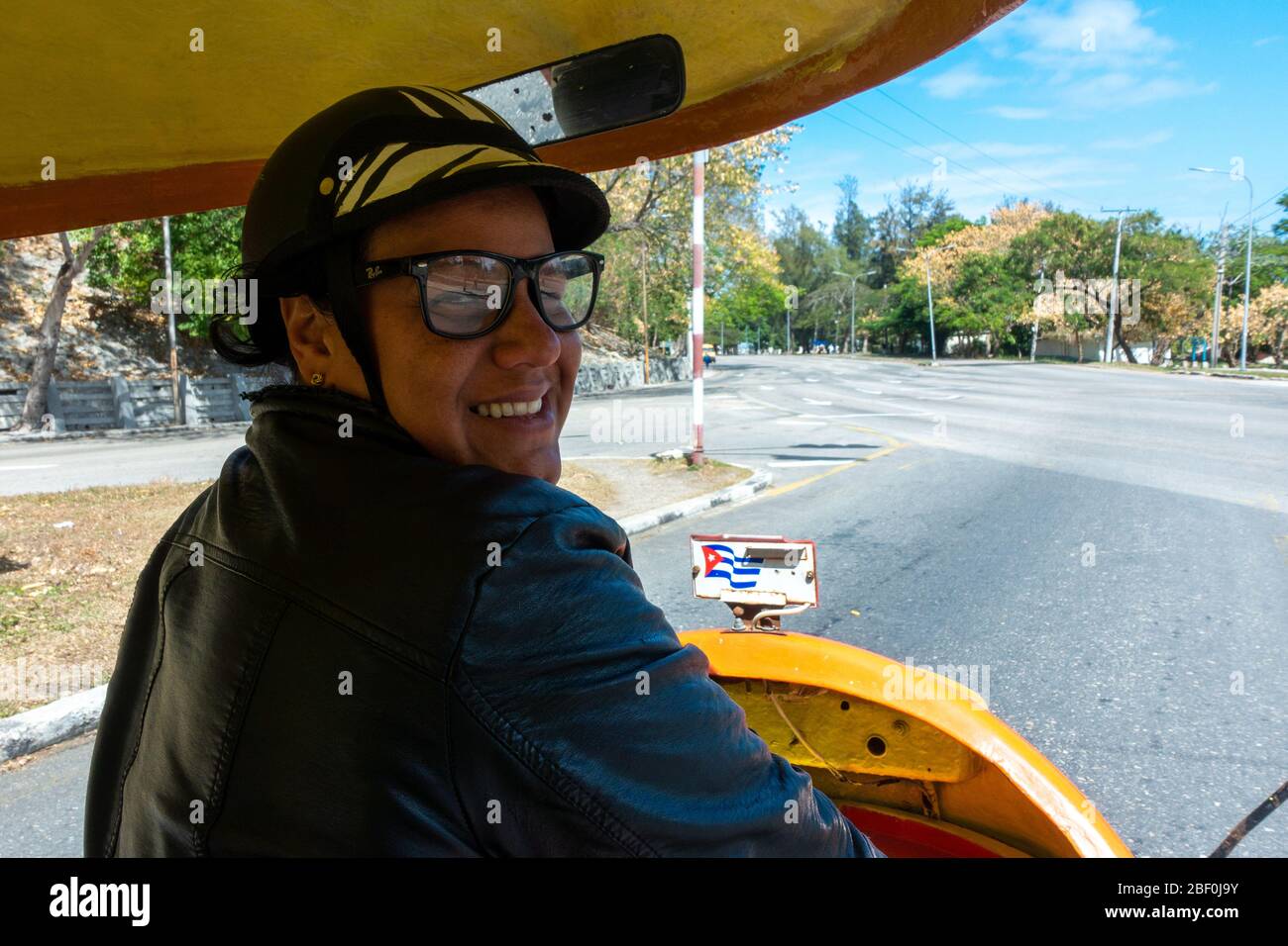 Freundliche gelbe Cocotaxi-Fahrerin (Moped Taxi) mit einem Lächeln zurück in die Altstadt von Havanna, Kuba Stockfoto