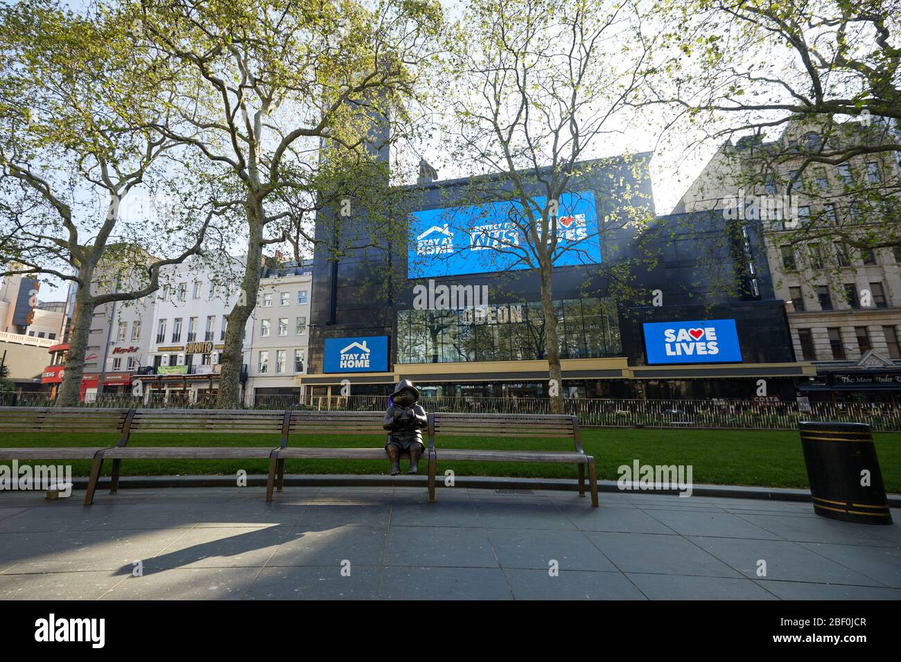 London, Großbritannien - 16 Apr 2020: Eine Statue des Paddington Bären auf einem verlassenen Leicester Square, vor Schildern, die Menschen ansagen, während der Sperrung der Coronavirus-Pandemie Covid-19 zu Hause zu bleiben. Stockfoto