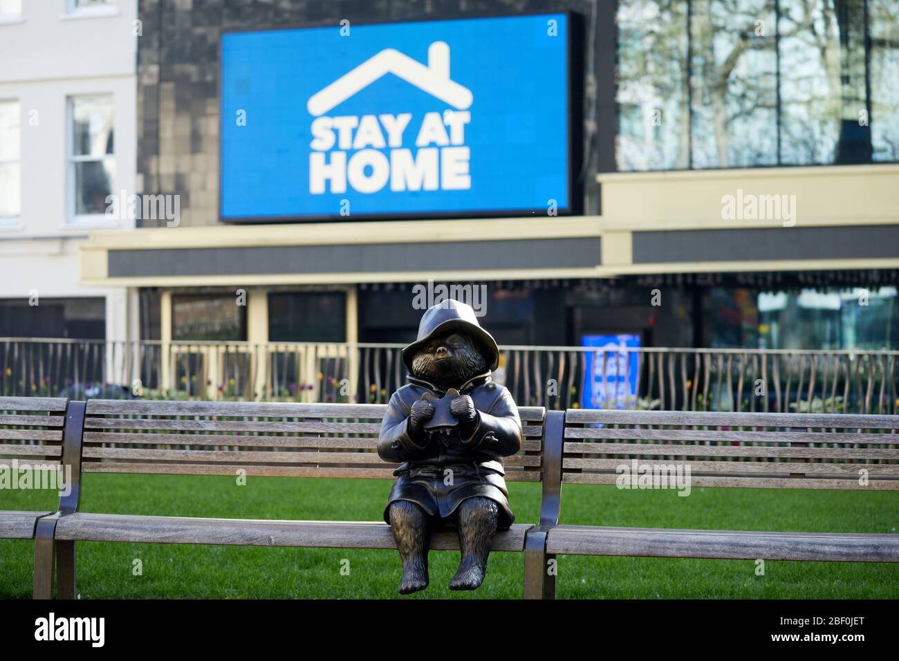 London, Großbritannien - 16 Apr 2020: Eine Statue des Paddington Bären am Leicester Square, vor einem Schild, das den Menschen aufzeigt, während der Sperrung der Coronavirus-Pandemie Covid-19 zu Hause zu bleiben. Stockfoto