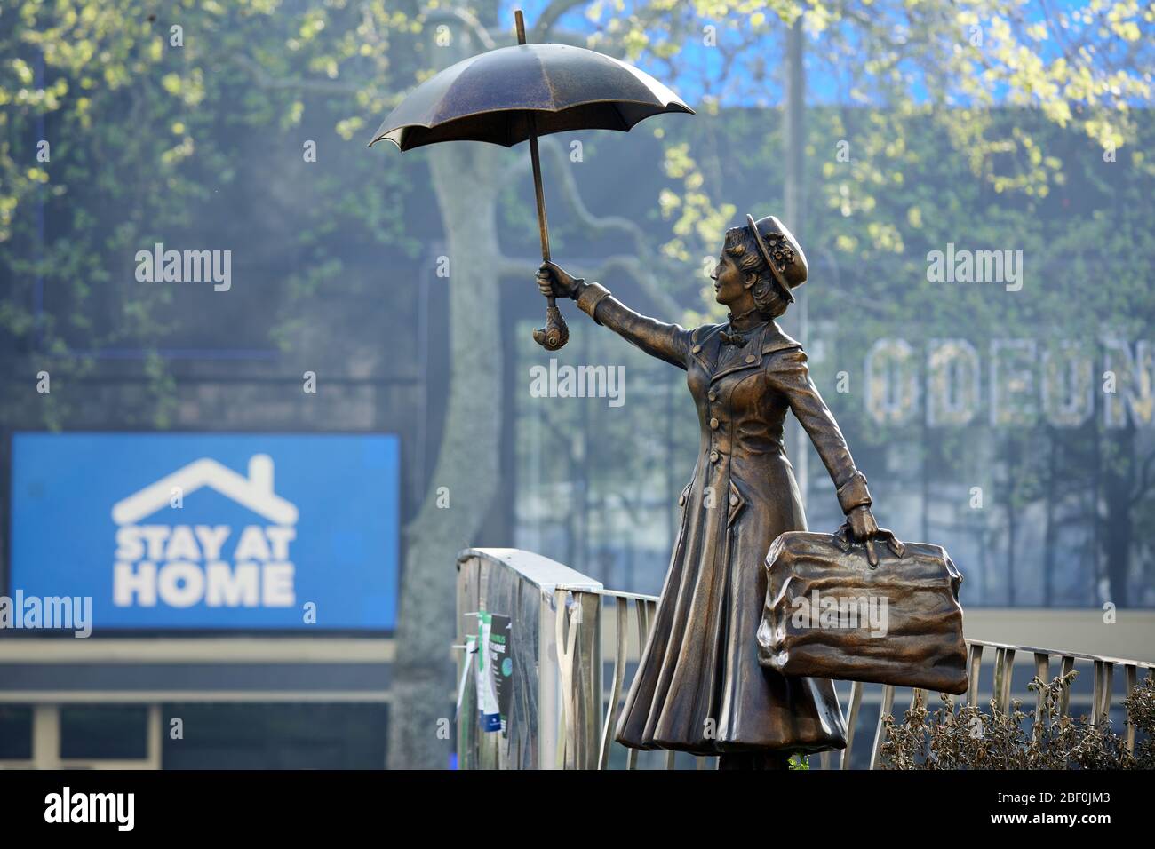 London, Großbritannien - 16 Apr 2020: Eine Statue von Mary Poppins am Leicester Square, vor einem Schild, das den Menschen aufzeigt, während der Sperrung der Coronavirus-Pandemie Covid-19 zu Hause zu bleiben. Stockfoto