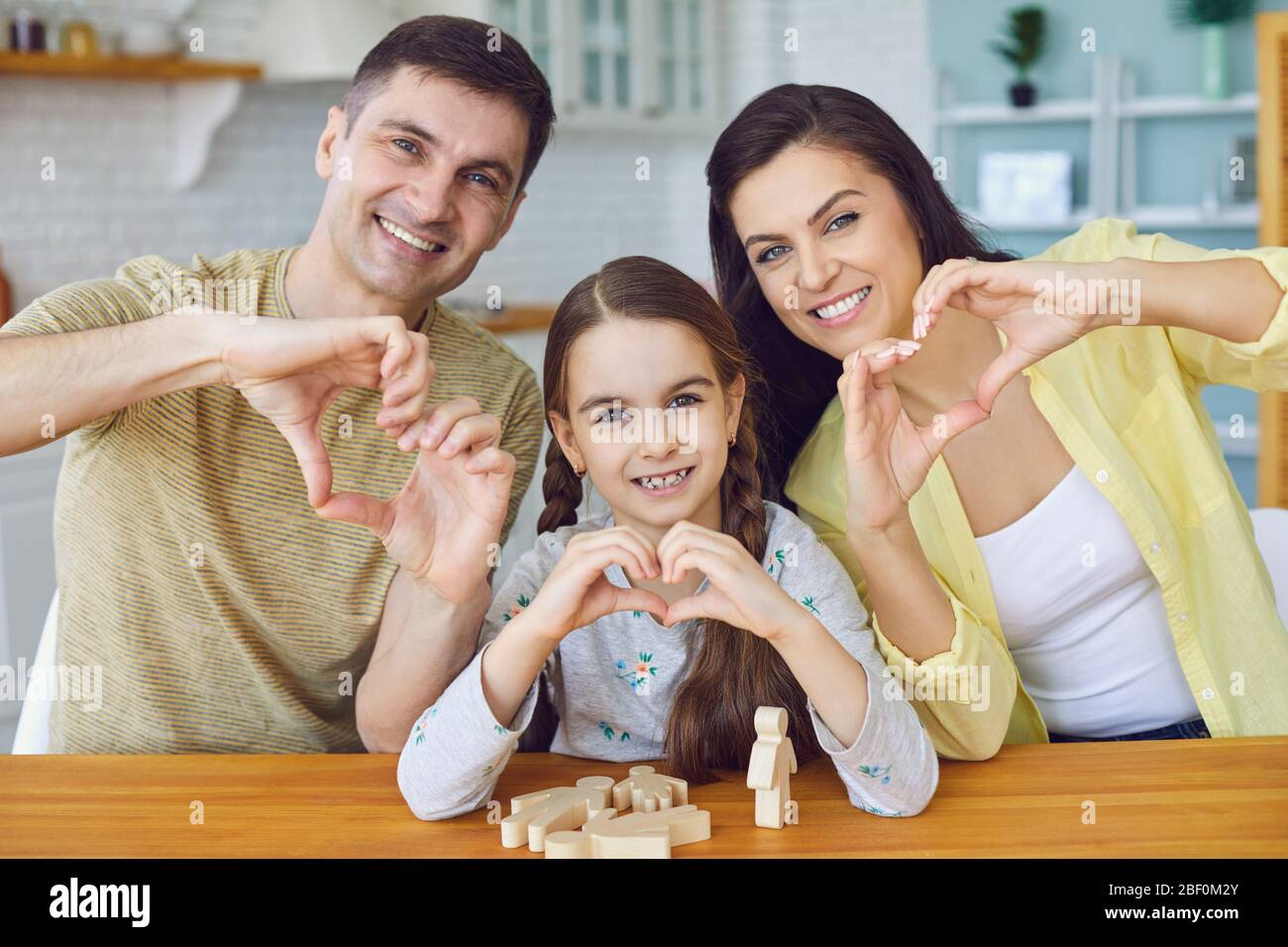 Glücklich lächelnd Familie hält Hände in der Form eines Herzens begrüßt sitzen an einem Tisch in der Küche im Haus Stockfoto