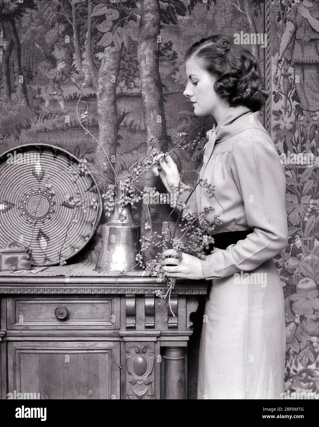 1930ER JAHRE BRÜNETTE FRAU ARRANGIEREN HERBST BEEREN IN KUPFER VASE NATIVE AMERICAN KORB UND KERAMIK AUF CREDENZA WANDTEPPICH AN DER WAND - F8163 HAR001 HARS KOPIEREN RAUM HALBE LÄNGE DAMEN PERSONEN PFLEGE VERTRAUEN KERAMIK B & W AUGE KONTAKT BRÜNETTE DEKORATION HAUSFRAU DEKOR HAUSFRAUEN STILE UND INTERIEURS HERBST SAISON HAUSFRAUEN GEHOBENE WANDTEPPICH WOHLHABENDE INNENARCHITEKTUR STILVOLLE NATIVE AMERICAN ARRANGIEREN BEEREN KUPFER KREATIVITÄT CREDENZA MODEN BLUME ARRANGIEREN WOHNKULTUR GUT ZU TUN JUNGE ERWACHSENE FRAU HERBSTLICH SCHWARZ UND WEISS KAUKASISCHEN ETHNIZITÄT HERBST LAUB MÖBEL HAR001 ALTMODISCH Stockfoto