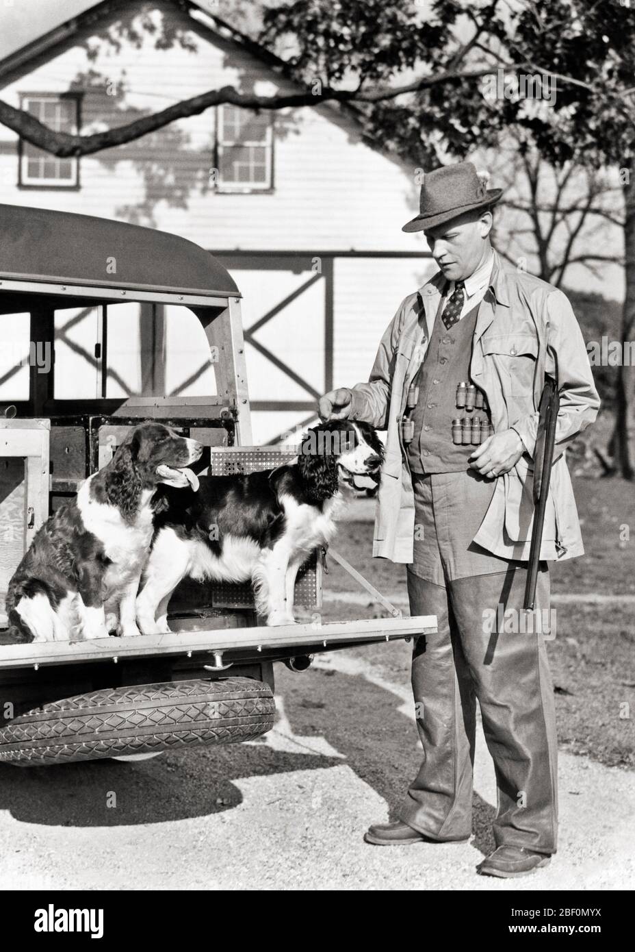 1930ER JAHRE MANN IN SCHIESSWESTE SCHROTFLINTE UNTER SEINEM ARM UND 2 SPRINGER SPANIEL HUNDE AUF DER RÜCKSEITE VON 1938 PLYMOUTH HOLZ KÖRPER KOMBI - G3126 HAR001 HARS LIFESTYLE SCHEUNE LÄNDLICHE HAUS LEBEN LUXUS KOPIE RAUM FREUNDSCHAFT VOLLER LÄNGE PERSONEN AUTOMOBIL MÄNNER HUNTER VERTRAUEN TRANSPORT WESTE B & W GESCHICKLICHKEIT AKTIVITÄT UNTERHALTUNG PLYMOUTH SÄUGETIERE ABENTEUER SEIN HOBBY FREIZEIT HOSEN INTERESSE UND AUTOS HUNDE HOBBIES WISSEN ERHOLUNG ZEITVERTREIB VERGNÜGEN SPRINGER POOCH WOODIE KOMBI 1938 AUTOMOBILE STILVOLLE FAHRZEUGE VOGELHUNDE HUNDE FEUERWAFFEN SÄUGETIER MITTE ERWACHSENE MITTE ERWACHSENE MANN ENTSPANNUNG ZWEISAMKEIT Stockfoto