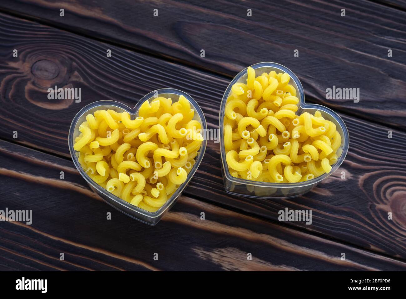 Trockene rohe Pasta auf dunklen Holzbrettern. Herzform, Symbol der Liebe, Kohlenhydrate Produkt. Zutat des Kochens. Makkaroni in zwei Schüssel auf braunem Holz ta Stockfoto