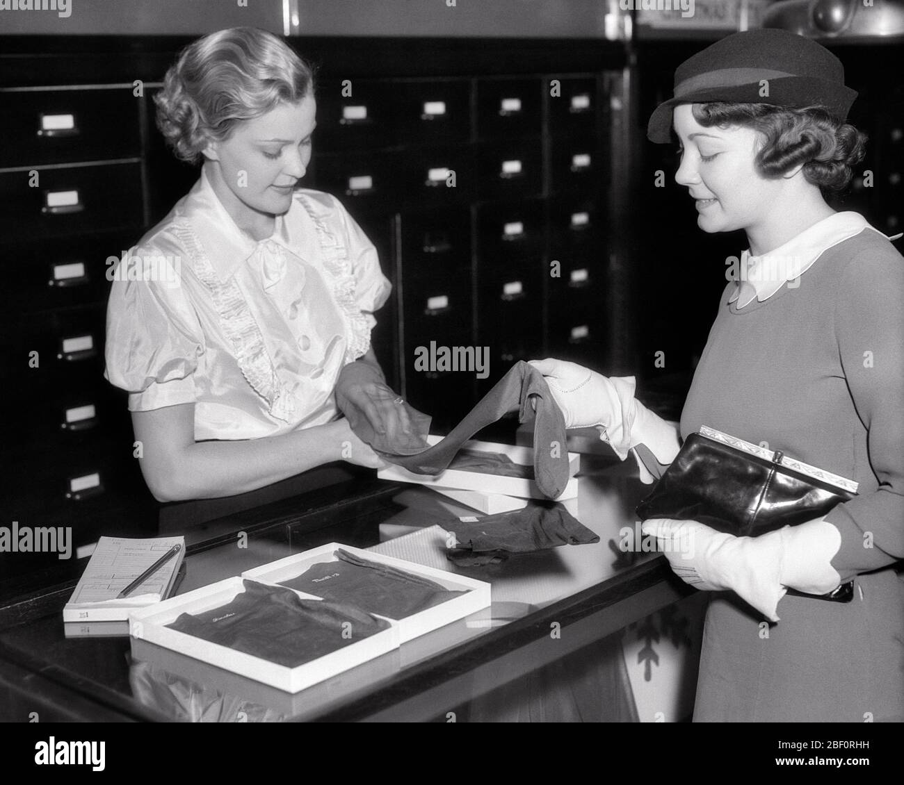 1930ER JAHRE VERKÄUFER HELFEN SHOPPER MIT EINER AUSWAHL VON STRUMPFWAREN SEIDENSTRÜMPFE - S5998 HAR001 HARS HALBE LÄNGE DAMEN PERSONEN FÜRSORGLICH VERTRAUEN B & W SHOPPER SHOPPER FÄHIGKEITEN BERUF FÄHIGKEITEN HIGH ANGLE KUNDENSERVICE BERUFE VERBINDUNG STRUMPFWAREN NYLONS AUSWAHL STILVOLLE ZUSAMMENARBEIT MITTE ERWACHSENE MITTE ERWACHSENE FRAU VERKÄUFER PROBEN JUNGE ERWACHSENE FRAU SCHWARZ UND WEISS KAUKASISCHE ETHNIZITÄT HAR001 ALTMODISCH SCHIERE Stockfoto