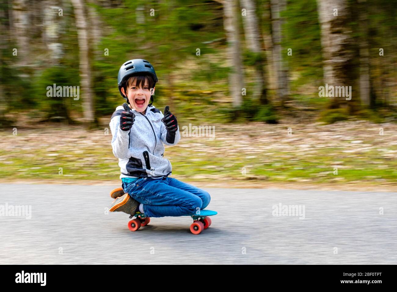 Junge, 9 Jahre alt, kniet auf einem Skateboard und lacht in die Kamera, Follower, Bayern, Deutschland Stockfoto
