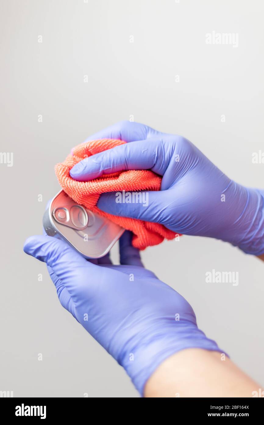 Handschuppen reinigen eine Dose Konserven nach dem Lebensmitteleinkauf, um die Ausbreitung des Coronavirus zu verhindern Stockfoto
