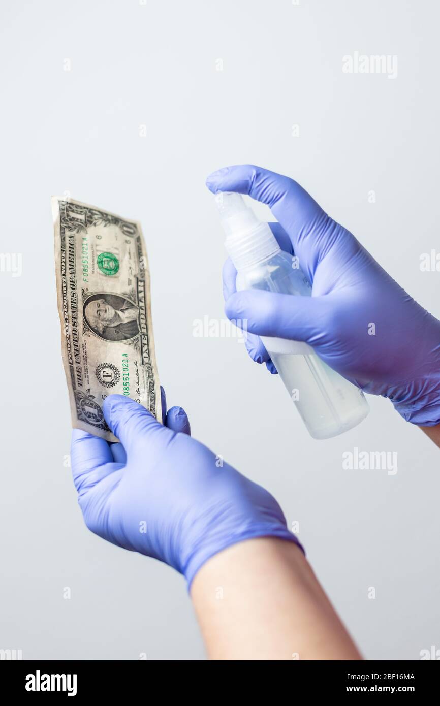 Handschuhliebte desinfizieren einen US-Dollar-Schein mit Alkoholspray, um die Ausbreitung des Coronavirus zu verhindern Stockfoto