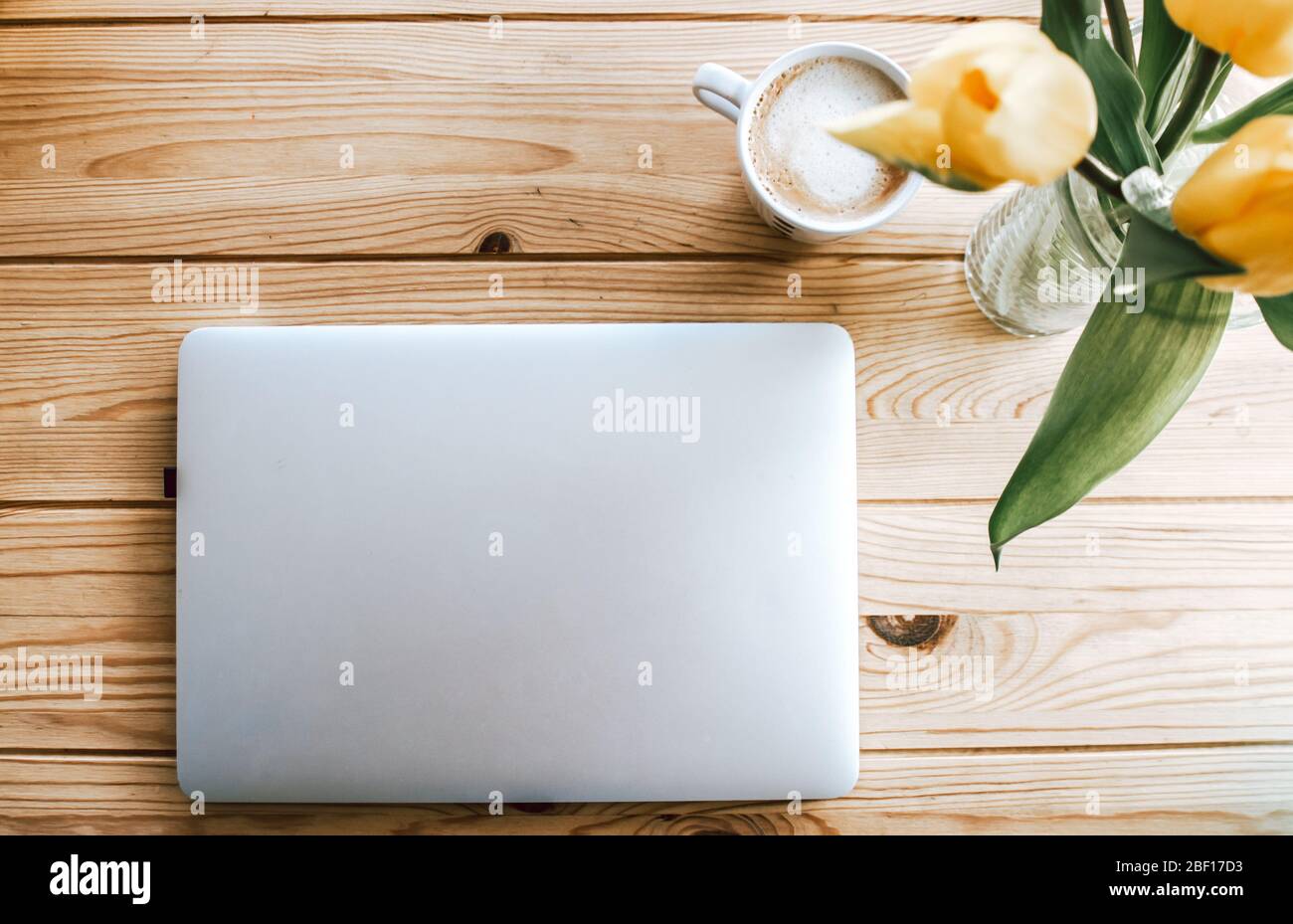 Schöner Arbeitsbereich. Holztisch mit Laptop, Kaffeebecher und gelben Blumen in einer Vase. Stockfoto