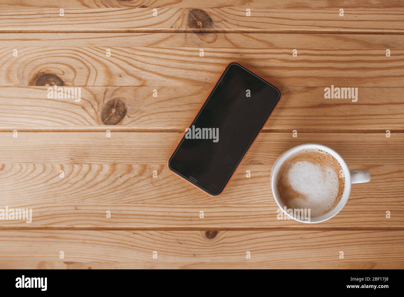 Smartphone und eine Tasse Kaffee auf einem Holzschreibtisch. Heller Holzhintergrund. Stockfoto