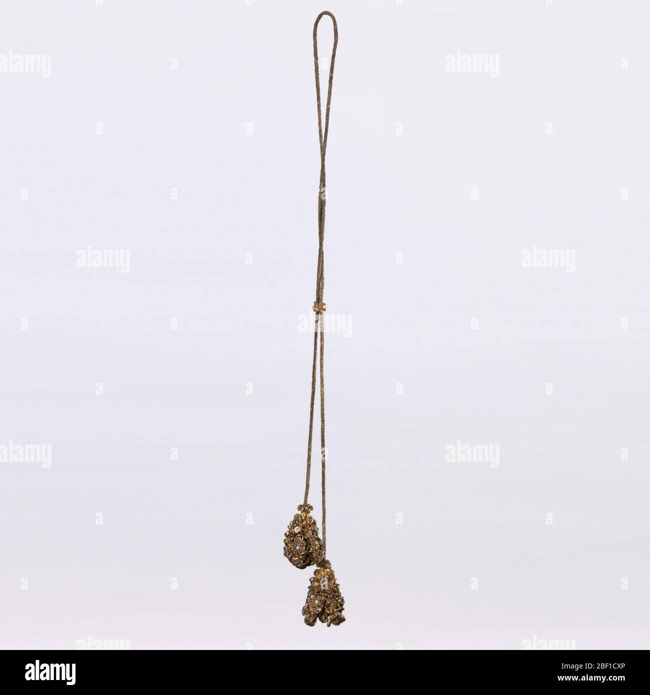 Kordel mit Quasten. Lond Schnur aus metallischem Faden, die an jedem Ende in einer kugelförmigen Quaste endet, gewellt, geloopt und stark mit Pailetten und Glassteinen besetzt. Stockfoto