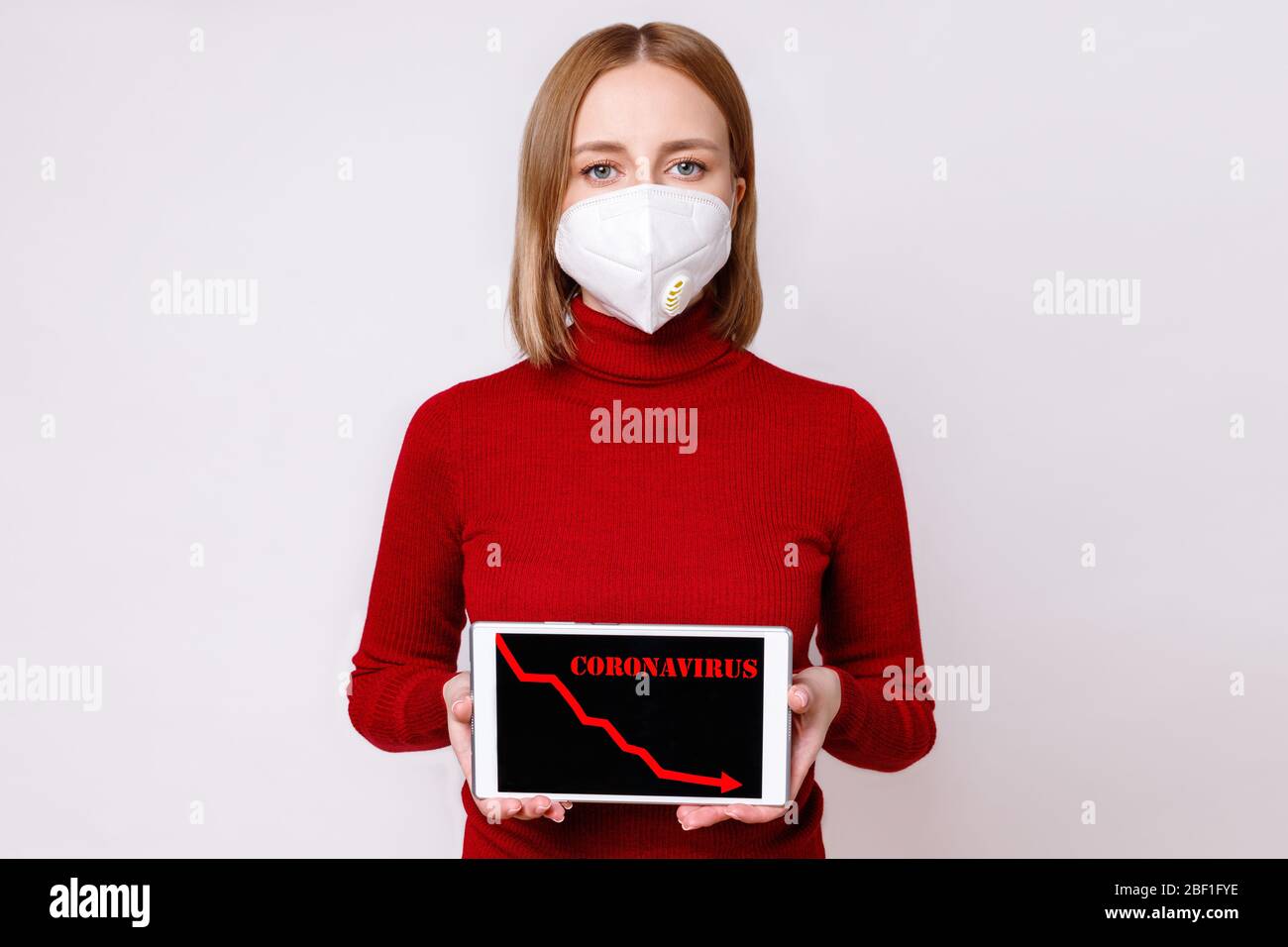 Europäische Frau trägt eine Gesichtsmaske, zeigt roten Pfeil nach unten, Rezession Prozess in der Wirtschaft auf digitalen Tablet, isoliert auf grauem Hintergrund. Co Stockfoto