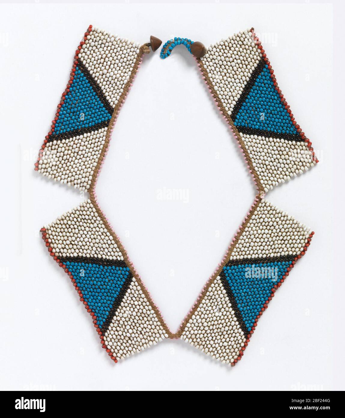 Halskette. Halskette bestehend aus vier rechteckigen Platten. Jedes hat ein weißes Feld mit einem blauen Dreieck, das in Schwarz eingefasst ist. Die obere Kante ist rosa und die untere Kante jedes Rechtecks ist rot. Mit konischen Metallknöpfen befestigt. Stockfoto
