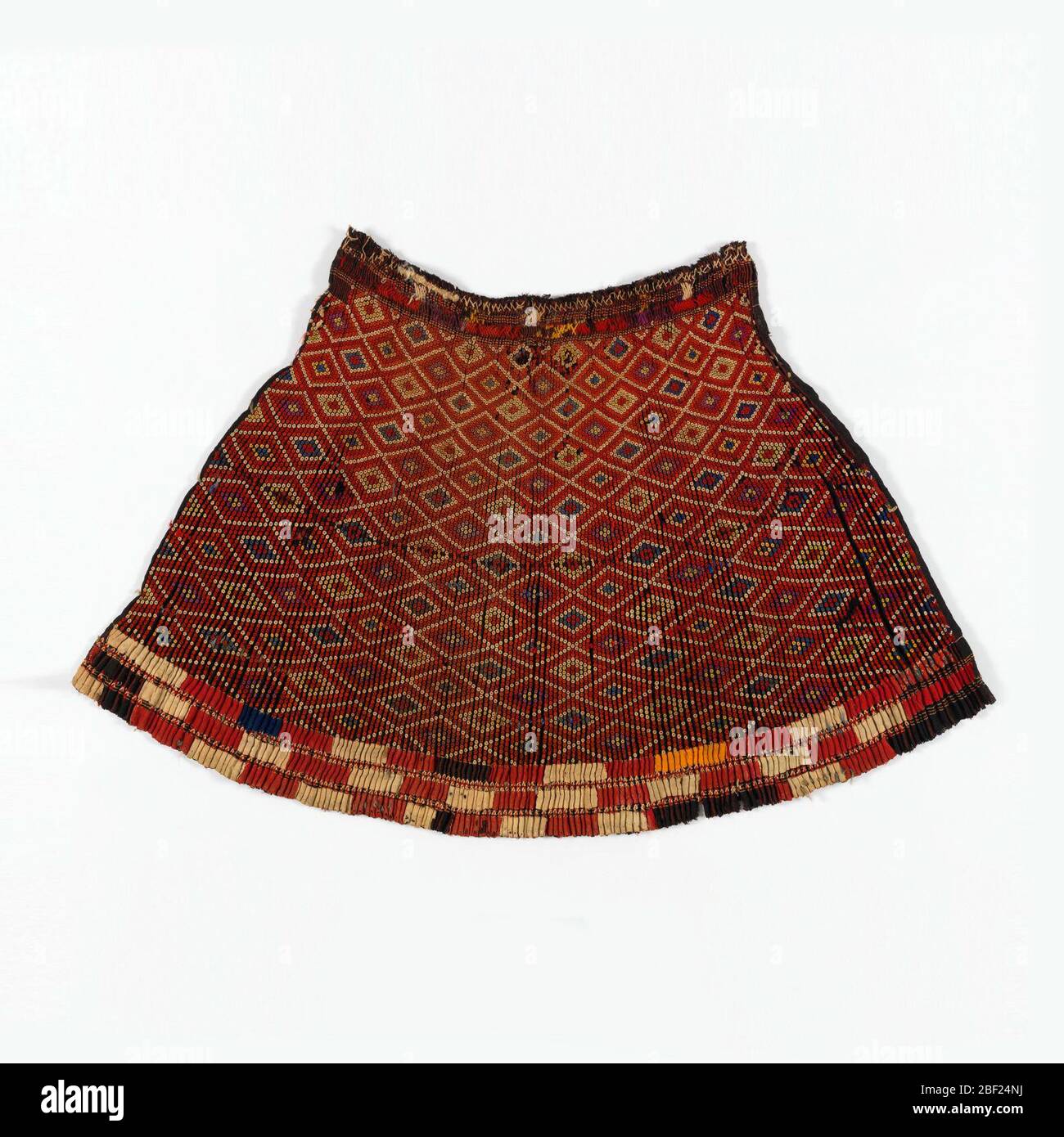 Rock. Schwarzes Leinen-Einfarbiges Tuch mit horizontalen Streifen aus Rot. Das Material ist eng gefaltet und die Falten durch Fäden gehalten; auf der Oberseite jeder Plissees ist ein Muster von winzigen Blumen bestickt in farbigen Wollen, angeordnet, um ein Rautenmuster zu bilden. Stockfoto