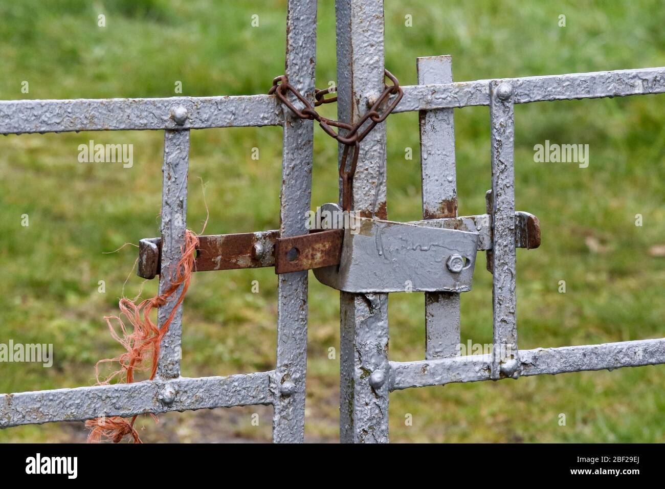 Alte Metall-Farm Tore durch Cross-Bar und orange Nylon Seil am Eingang zum Feld gesichert. Stockfoto