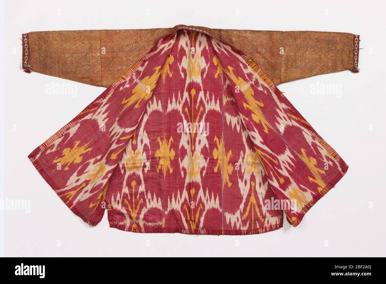 Chapan Robe. Robe mit ogivalen Gitter in Gold metallic auf einem Terrakotta-Seide Fundament gemustert. Kanten mit Strickseide in rot, blau, gelb, schwarz und weiß. Mit Seide und Baumwolle Warp ikat Stoff in rot, weiß und gelb gefüttert. Stockfoto