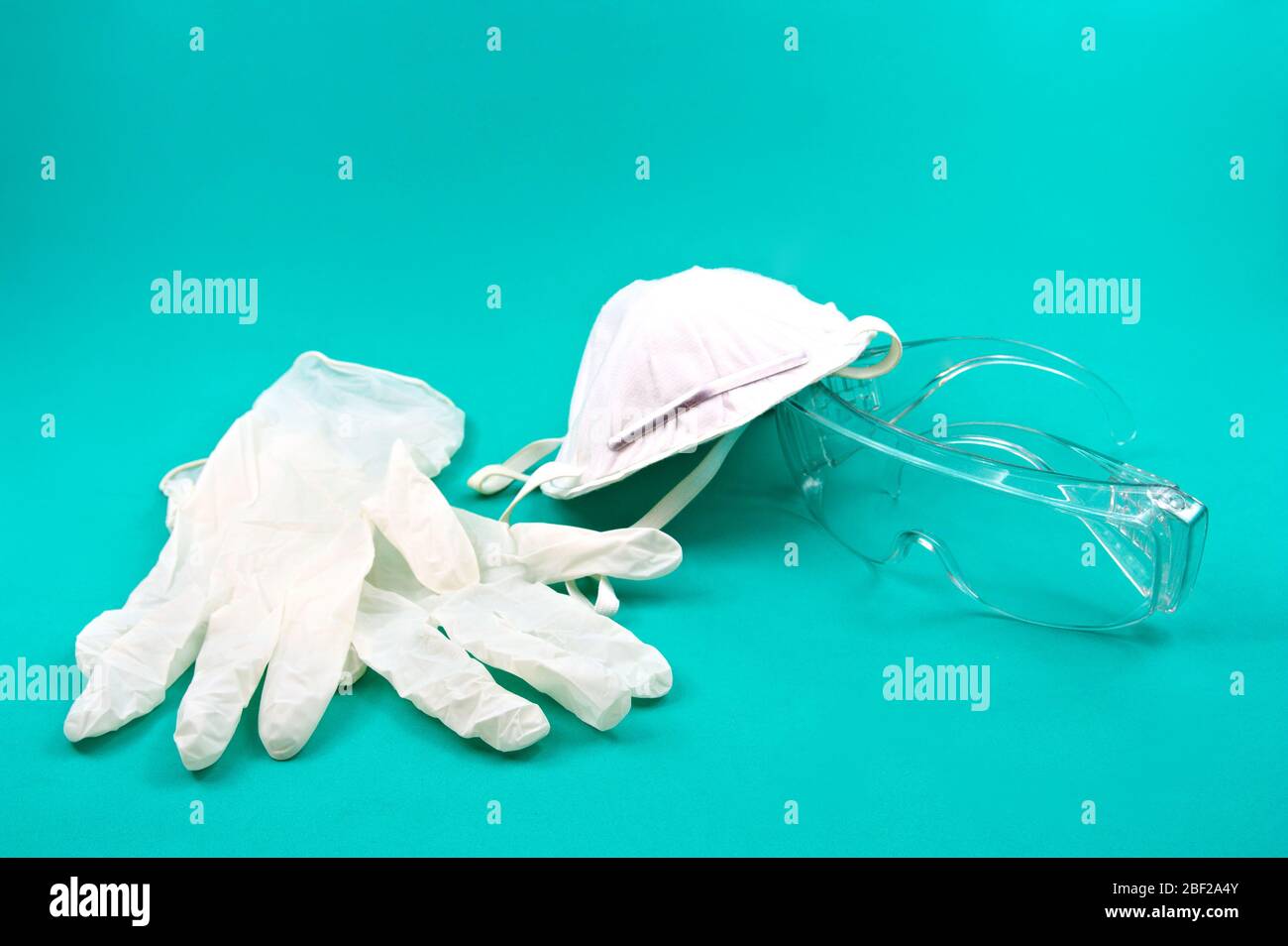 Eine Maske, Handschuhe und individuelle Schutzbrille, um die Ausbreitung von möglichen Viren, die in der Umwelt vorhanden sein können, zu verhindern, alle auf einem grünen Hintergrund Stockfoto