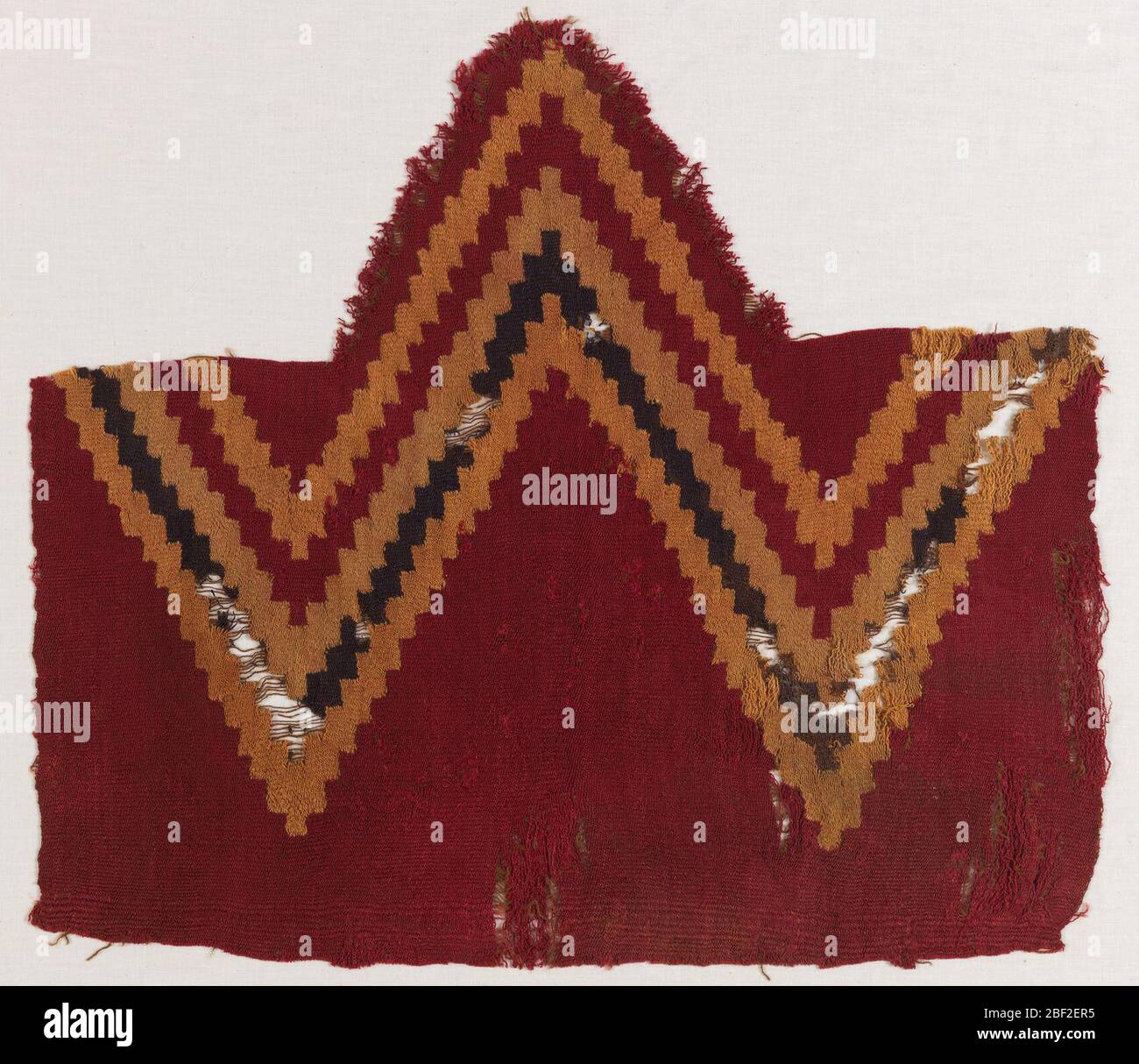 Fragment. Großes Zickzack-Design bestehend aus vier Reihen in den Farbtönen tan, dunkelblau, auf rotem Hintergrund. Stockfoto